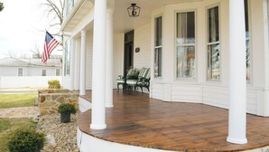 Een overdekte veranda met witte zuilen, een stenen plantenbak en een vlag.
