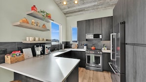 A modern kitchen with dark cabinetry, a large island, stainless steel appliances, and a rustic ceiling. - 3BR Mountain View Cabin | Private Hot Tub & Fire Pit | Lake & Resort Proximity | Sleeps 6 (Liberty)