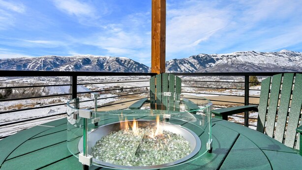 A glass-top outdoor seating area with a fire feature, overlooking a snowy mountain landscape. - 3BR Mountain View Cabin | Private Hot Tub & Fire Pit | Lake & Resort Proximity | Sleeps 6 (Liberty)