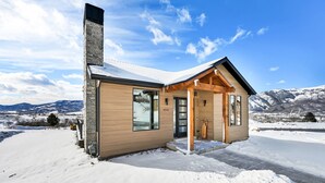 A snow-covered cabin with a wooden exterior, large windows, and a chimney. - 3BR Mountain View Cabin | Private Hot Tub & Fire Pit | Lake & Resort Proximity | Sleeps 6 (Liberty)