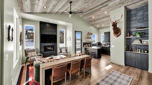 A spacious living area with a fireplace, dining table, and chairs. - 3BR Mountain View Cabin | Private Hot Tub & Fire Pit | Lake & Resort Proximity | Sleeps 6 (Liberty)