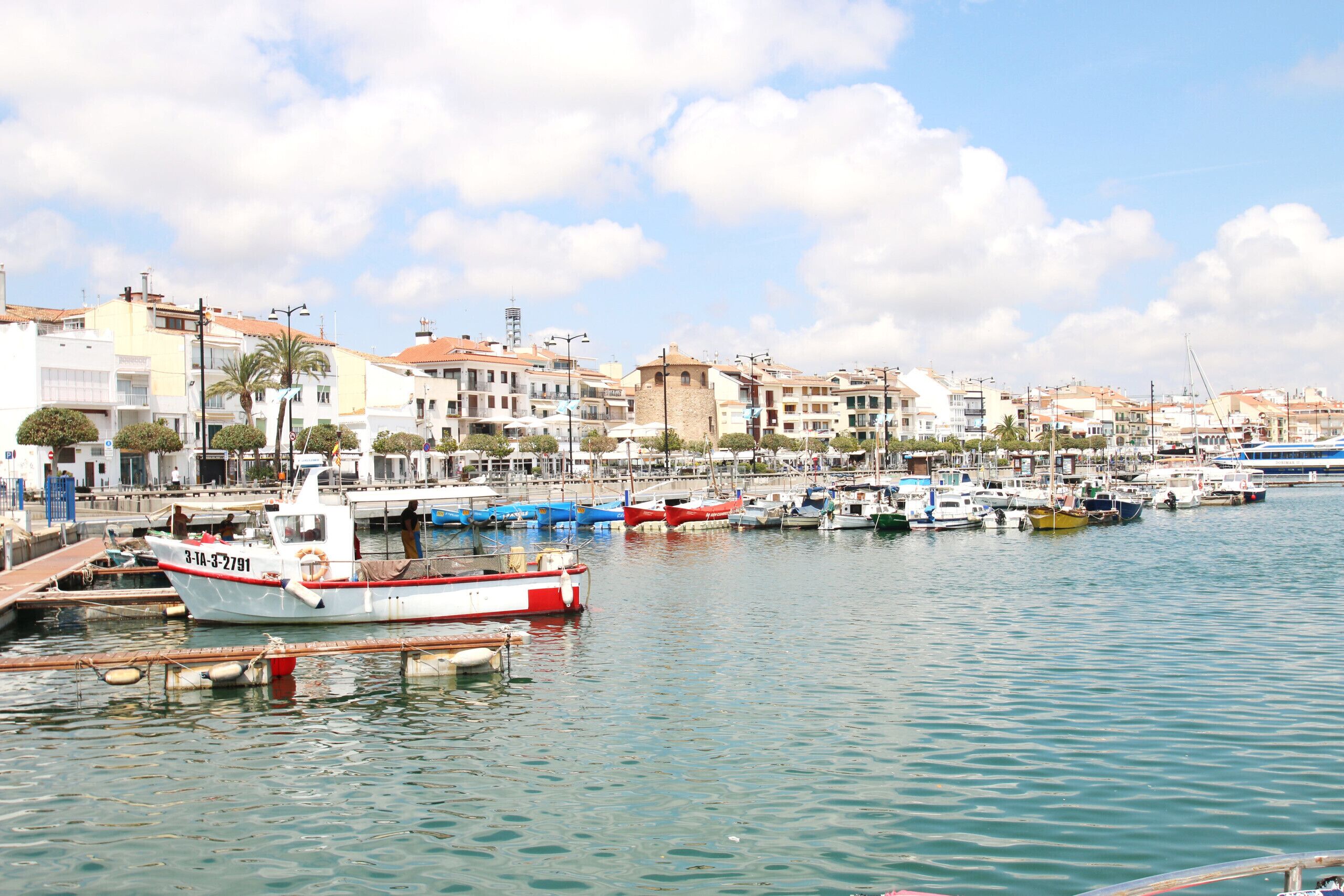 A marina with boats docked, a clear sky, and buildings in the background.