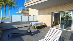 Terraço no telhado com mesa posta para refeições, uma cadeira de lounge e vista dos edifícios e palmeiras ao redor.