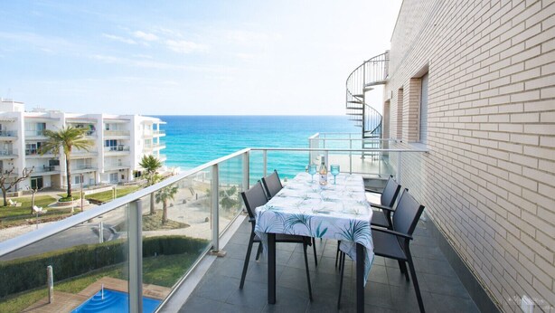 Un balcón con mesa y sillas con vista al mar, junto a un edificio de fachada de ladrillo.