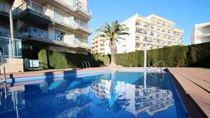 Una piscina con una vista despejada de edificios cercanos, incluyendo una construcción de varios pisos con balcones y una palmera.