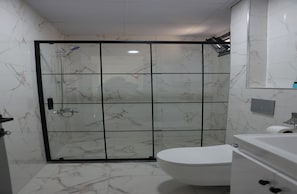 A bathroom with a glass-enclosed shower, a toilet, and a sink.