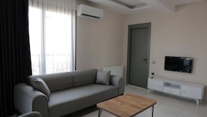 A modern living room with a grey sofa, a wooden coffee table, a TV on a white cabinet, and an air conditioning unit on the wall. - IMPERIUM RESORT HOTEL (Erdemli)
