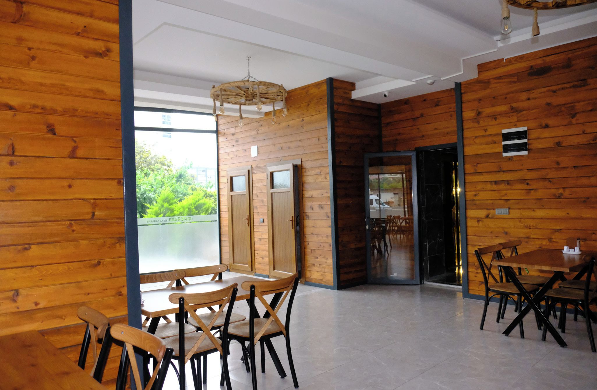 Ein modernes Interieur mit Holzwandverkleidung, einem Essbereich mit Holztischen und -stühlen und Blick durch eine Glastür.