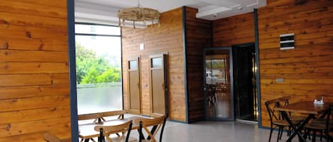 Un interior moderno con paneles de madera, una zona de comedor con mesas y sillas de madera, y vistas a través de un ventanal.