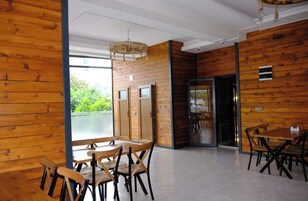 A modern interior with wooden panel walls, a dining area with wooden tables and chairs, and a view through a glass door.
