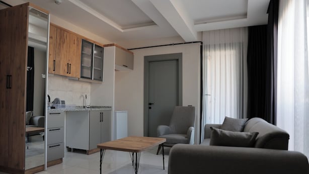A modern living room with a sofa, a coffee table, and a dining area with a kitchen in the background. - IMPERIUM RESORT HOTEL (Erdemli)