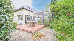 Uma casa moderna com um pátio, uma estufa de vidro e um jardim com cascalho e plantas.