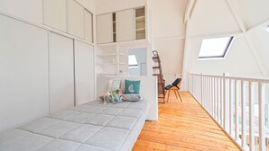 Quarto estilo loft com cama, uma cadeira e claraboia.