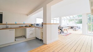 Cozinha moderna com armários brancos, bancada de madeira e micro-ondas. Possui uma área de jantar com mesa e cadeiras, e uma grande janela que proporciona iluminação natural.