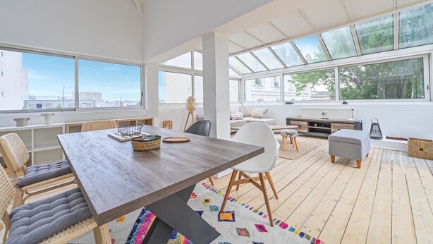 Uma sala de estar ampla com uma mesa de madeira, assentos confortáveis e grandes janelas com vista para a cidade.