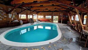 En indendørs swimmingpool med trævægge og -loft, omgivet af bænke og borde.