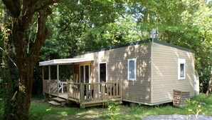 A small, single-story cabin with a porch and a covered entryway, surrounded by trees. - ZEcamping 3 étoiles piscine pet friendly mobil-home TV LV clim 29m2 (Urt)