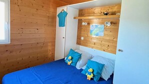 Una habitación con paneles de madera, una cama, un armario blanco y una ventana.