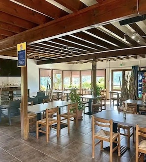 Un comedor interior con mesas y sillas de madera, ventanas amplias y un techo alto con vigas a la vista.