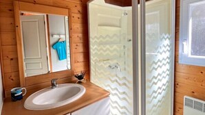 Baño de cabaña de madera con lavamanos blanco, un espejo y ducha con puerta de vidrio con diseño en zigzag.