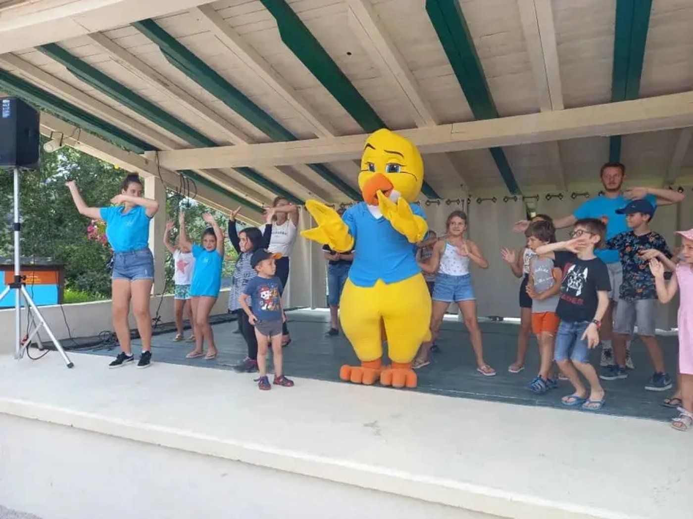 A group of people on a covered outdoor stage with a large inflatable duck mascot.