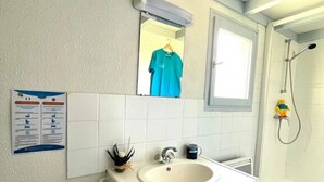 Ein Badezimmer mit einem weißen Waschbecken, einem Spiegel, einem Handtuchhalter und einer Dusche.