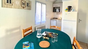 Eine gemütliche Küche mit Esstisch für zwei Personen, einem Kühlschrank und einem Fenster mit Vorhängen.