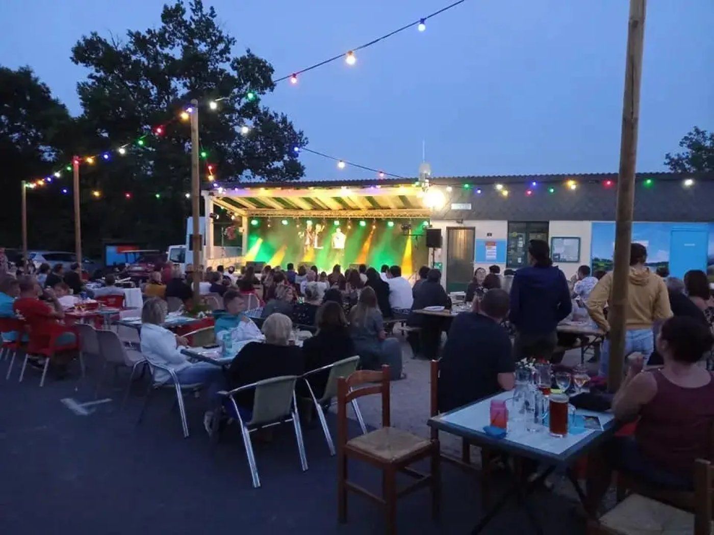 An outdoor event with a stage and audience seated at tables.