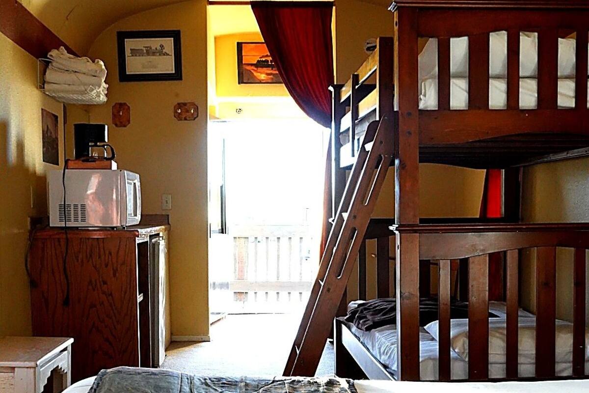 A room with bunk beds, a desk with a microwave, and a window with curtains.