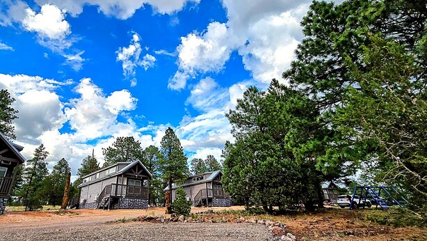 A cabin-style lodging area with multiple wooden cabins, surrounded by trees and a clear sky. - Railcar on Historic Route 66 (Williams)