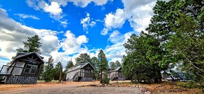 A cabin-style lodging area with multiple wooden cabins, surrounded by trees and a clear sky. - Railcar on Historic Route 66 (Williams)
