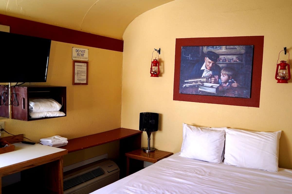 A hotel room with a bed, a desk, a television, and a painting on the wall.