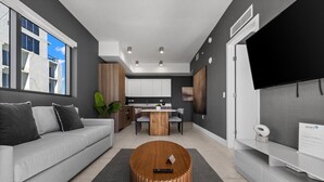 A modern living room with a sofa, a coffee table, a TV, and a kitchen area in the background.