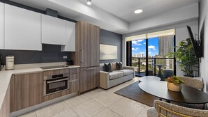 A modern kitchen with built-in appliances, a grey sofa, and a dining area with a table and chairs.