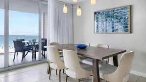 A dining area with a large table and chairs, a view of the ocean through a glass door, and a blue abstract painting on the wall. - Luxurious 2 BRD/2BATH  Suite in serene Marco Island (Marco Island)