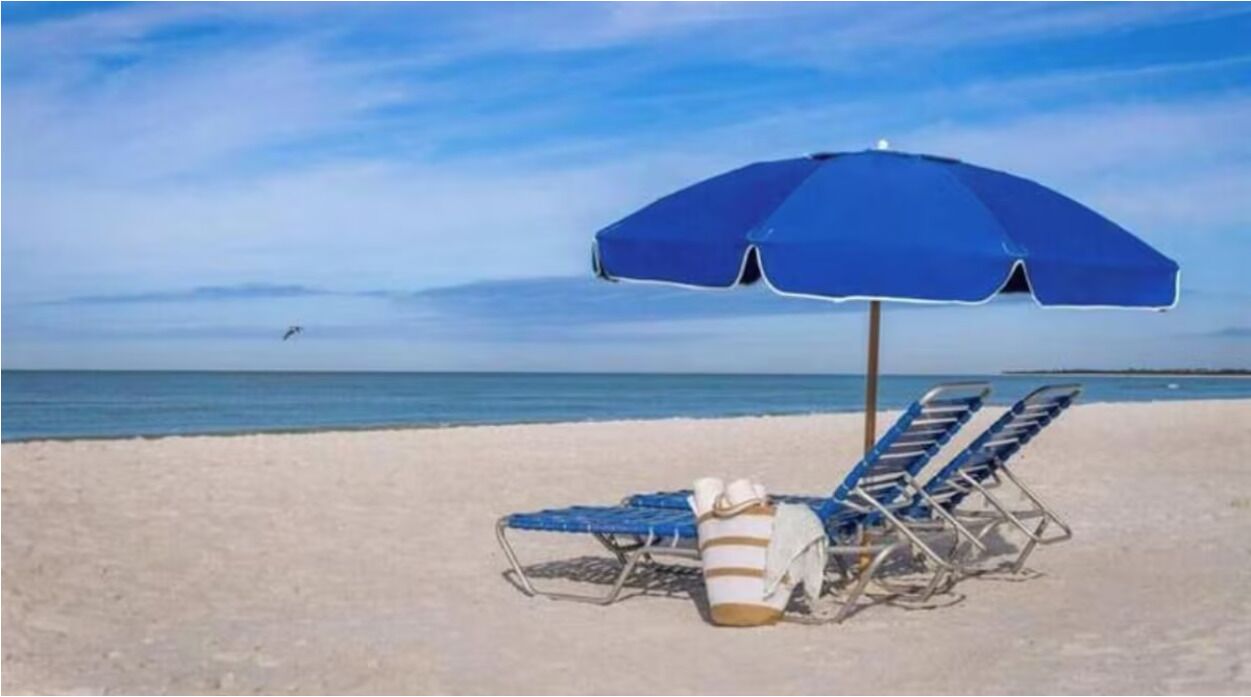 Cena de praia com um guarda-sol azul, duas espreguiçadeiras e um balde.
