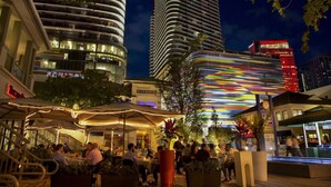 A nighttime urban scene with a dining area, high-rise buildings, and a brightly lit structure. - Modern Studio with Balcony in Brickell (Miami)