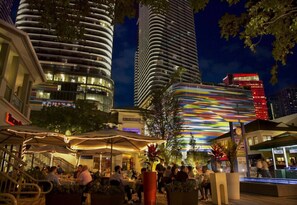 A nighttime urban scene with a dining area, high-rise buildings, and a brightly lit structure. - Modern Studio with Balcony in Brickell (Miami)