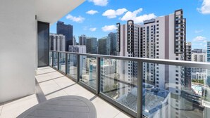 A balcony with a glass railing overlooking a cityscape with high-rise buildings. - Modern Studio with Balcony in Brickell (Miami)
