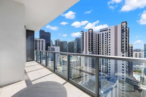 Ein Balkon mit Glastrennwand und Blick auf eine Skyline mit Hochhäusern.