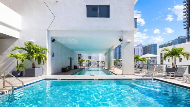 A swimming pool with a view of tall buildings, surrounded by lounge chairs and palm trees. - Modern Studio with Balcony in Brickell (Miami)