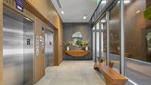 A modern elevator area with metallic doors, a wooden reception desk, and a bench. - Modern Studio with Balcony in Brickell (Miami)