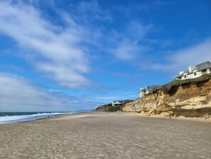Une plage avec des maisons construites sur une falaise, un ciel dégagé et l’océan en toile de fond.