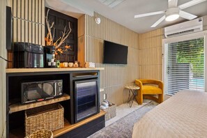 A modern hotel room with a flat-screen TV mounted on the wall, a microwave, a small oven, a wicker basket, a yellow armchair, and a bed with a quilted cover. - Exclusive use of the property (All 5 units) (Palm Springs)
