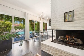 Ein modernes Wohnzimmer mit Kamin, Blick auf einen Pool und einem Essbereich mit Glastischen.