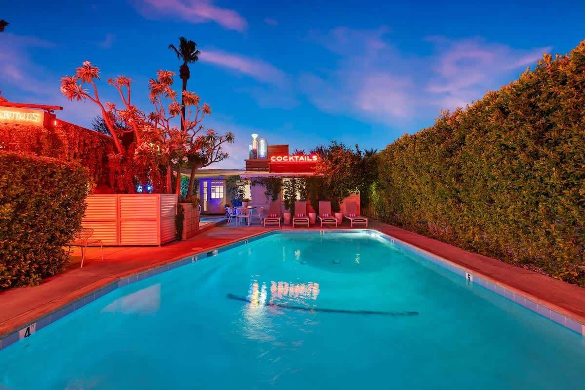 Una piscina con zona de bar, sillones de descanso y un seto.