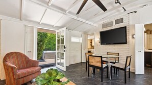 A modern living room with a sofa, dining table, chairs, and a TV mounted on the wall. - Adobe Cottage; Unit A (Palm Springs)