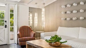 A modern living room with a white sofa, a striped armchair, a wooden coffee table, and a wall-mounted light fixture. - Adobe Cottage; Unit A (Palm Springs)