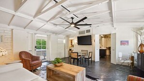 A spacious living area with a high ceiling, a ceiling fan, a wooden coffee table, a striped sofa, and a television mounted on the wall. - Adobe Cottage; Unit A (Palm Springs)