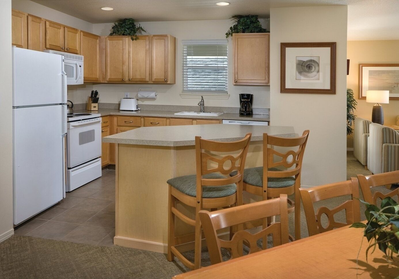 A compact kitchen with wooden cabinets, a white refrigerator, a stove, and a sink. There is a dining area with a table and chairs.